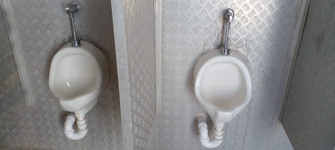 Wall-mounted urinals with chrome flush fittings and plumbing connections