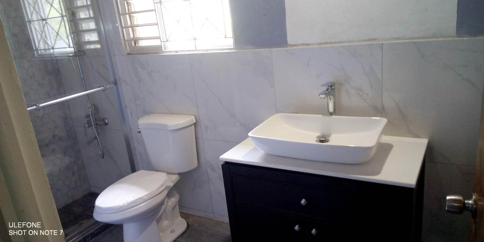 Renovated bathroom with marble-look tile, vessel sink on a dark wood vanity and walk-in shower